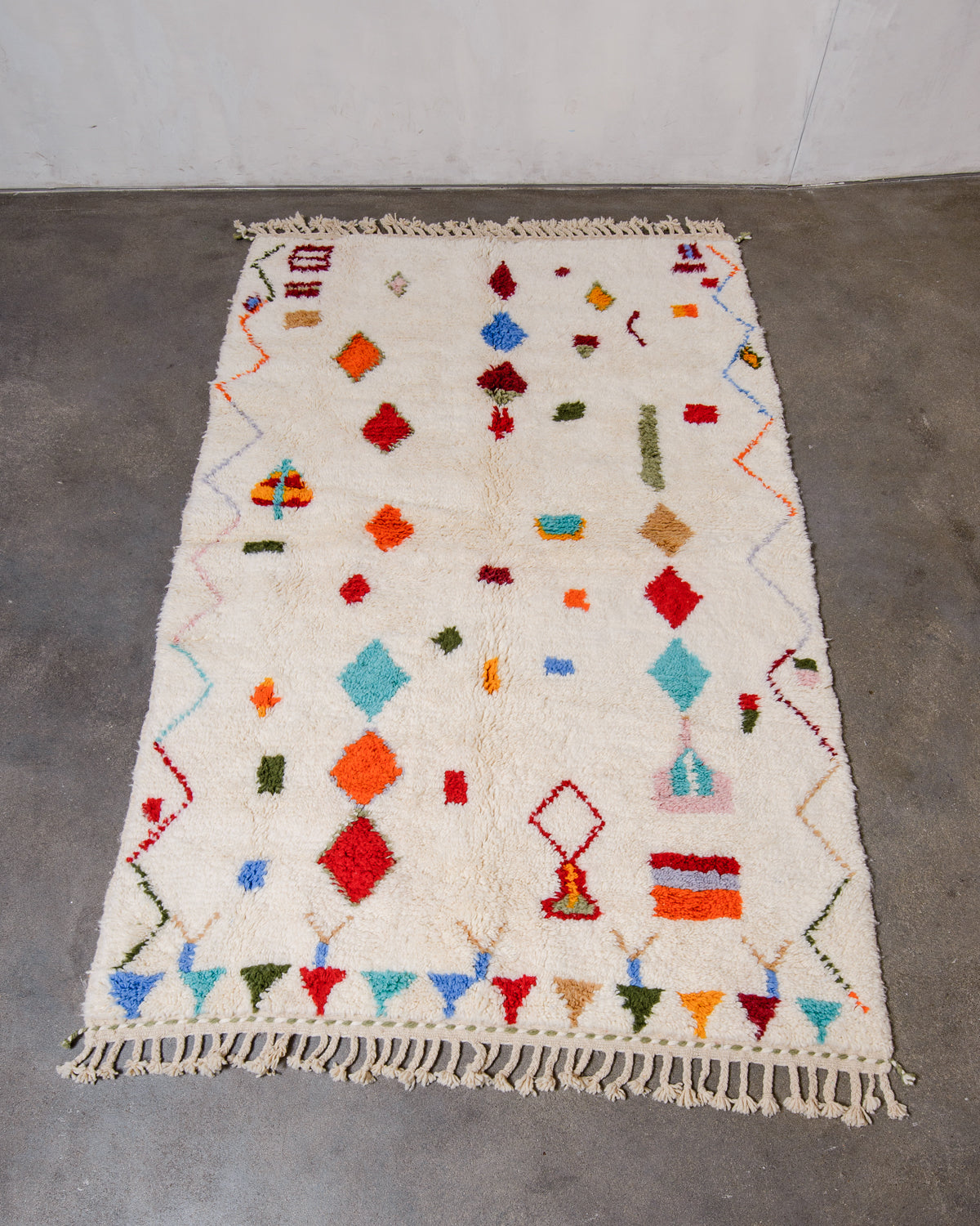 Berberlin Beniourain rug in cream wool with colourful motifs, laying flat on concrete studio floor.